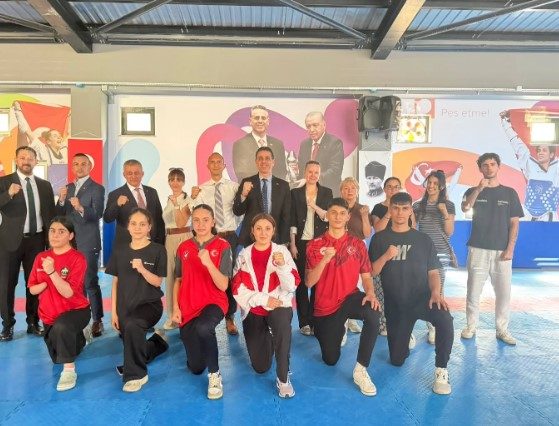 Spor salonunda proje heyeti ve eşofmanlı millî sporcular birlikte poz veriyor.